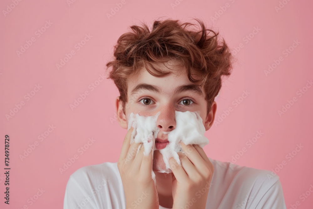 Handsome nervous teenage boy with foam on face learning to shave isolated on pink studio background Handsome nervous teenage boy with foam on face learning to shave isolated on pink studio background