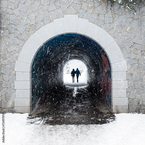 A silhoette of a romantic couple holding hands on a winter walk for the Valetines dinner walking through a dark pedestrian tunnel to white snowy garden. Light at the end of  the tunnel. 