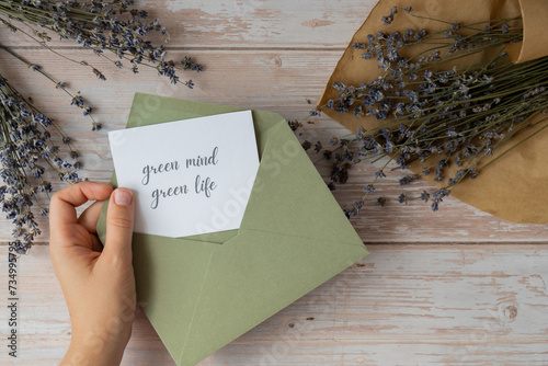 Female hands taking paper card note with text GREEN MIND GREEN LIFE from envelope. Lavender flower. Top view, flat lay. Concept of eco sustainability lifestyle mental spiritual health photo