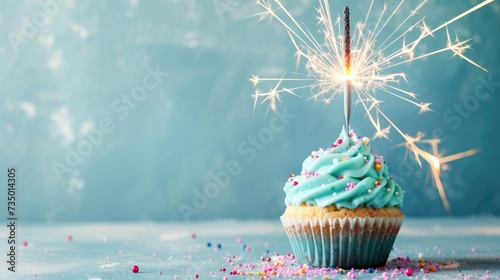 A beautifully decorated cupcake topped with blue icing, colorful sprinkles, and a lit sparkler represents a festive celebration, possibly a birthday or special event.