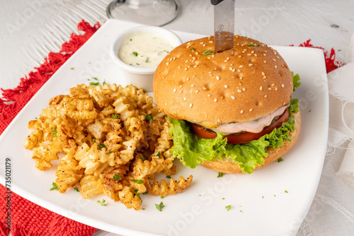 Hamburguesa artesanal hecha con torta de carne angus a la parrilla y deliciosa salsa, acompañada de papas caseras sobre plato blanco