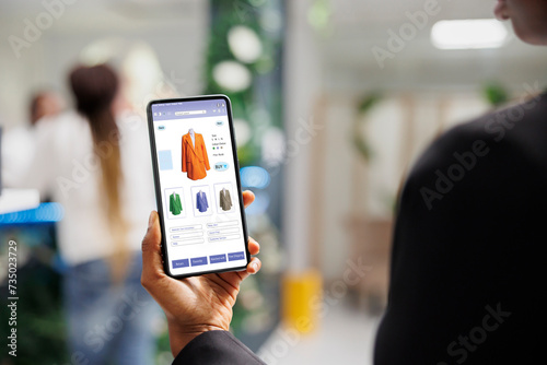 Client using clothing online web store application on smartphone, reviewing fashion items and buying products. African american woman looking at trendy clothes line on digital shop.