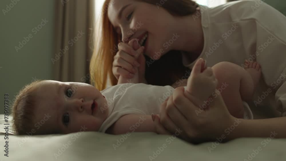 Mom and baby playing feeling joy. Happy joyful satisfied smiling woman kissing baby girl, stroking, caressing, kissing legs, hands, tummy of cute little newborn baby kid child on bed. Atmospheric Shot Mom and baby playing feeling joy. Happy joyful satisfied smiling woman kissing baby girl, stroking, caressing, kissing legs, hands, tummy of cute little newborn baby kid child on bed. Atmospheric Shot