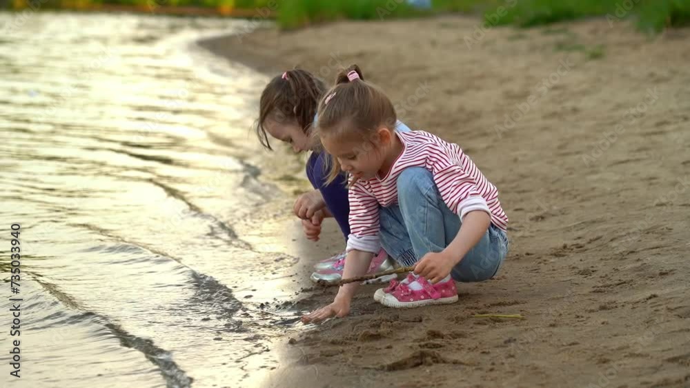 Happy little girls play with sand and water on river in summer park. Active childrens leisure games. Outdoors Happy little girls play with sand and water on river in summer park. Active childrens leisure games. Outdoors