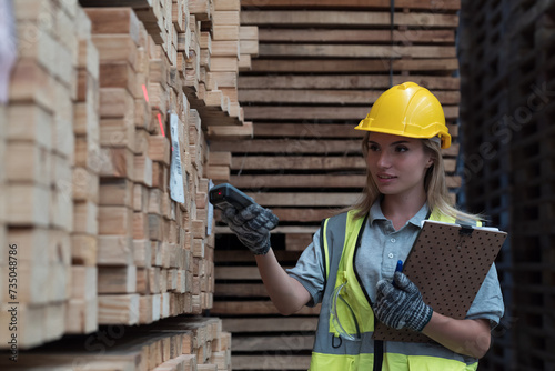 Woman warehouse worker scanning barcodes on pile of plank wooden in lumber storage warehouse. Woman worker worker checks barcodes on pile of plank wooden in wooden warehouse