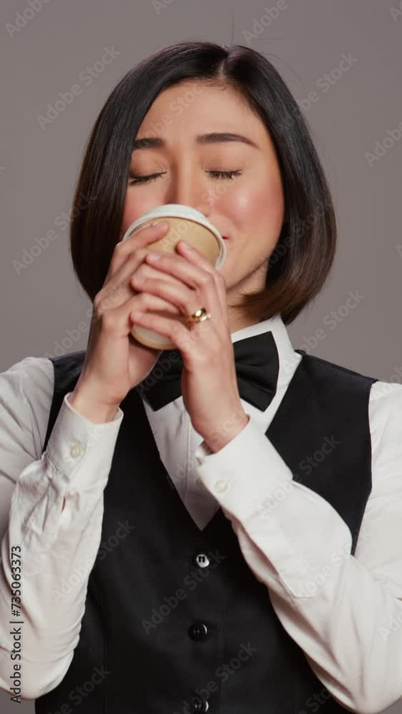 Vertical Video Asian receptionist serving coffee cup in front of camera, taking a break and enjoying hot refreshment. Hotel administrator drinking caffeine beverage, tourism concept. Camera B. Vertical Video Asian receptionist serving coffee cup in front of camera, taking a break and enjoying hot refreshment. Hotel administrator drinking caffeine beverage, tourism concept. Camera B.