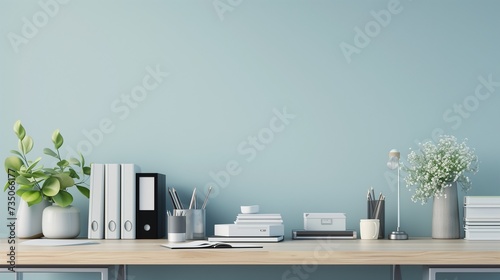 A modern office desk set against a pale blue wall, neatly arranged with books and supplies, and ample copy space for text or product display.