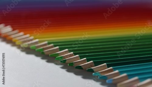 Colored pencils lie in a row on the table  close-up  blurry. Color palette from green to red. Education