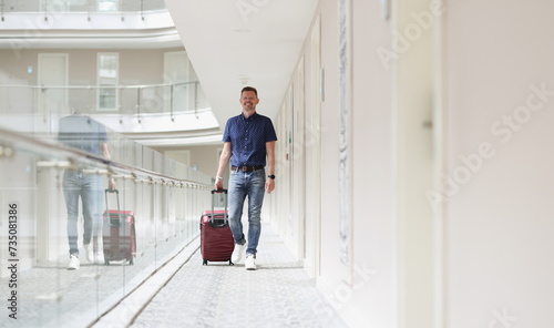 A man with a suitcase walks along the floor of the hotel. Accommodation, summer vacation in a resort alone