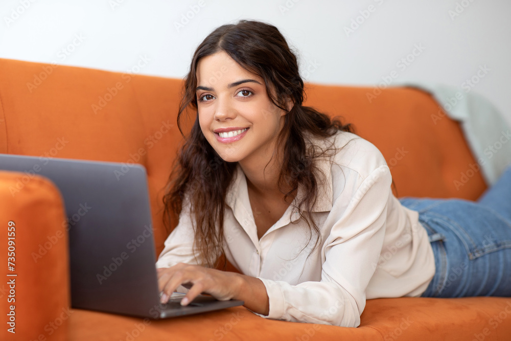 Smiling Woman Browsing Internet On Laptop While Relaxing On Couch At Home Smiling Woman Browsing Internet On Laptop While Relaxing On Couch At Home