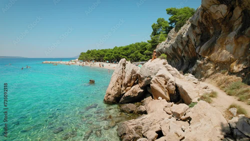 Woman relaxing on rocky beach. Croatia's pebbly paradise beckons. Makarska Riviera by rugged mountains and dotted with sunbathers. Woman relaxing on rocky beach. Croatia's pebbly paradise beckons. Makarska Riviera by rugged mountains and dotted with sunbathers.