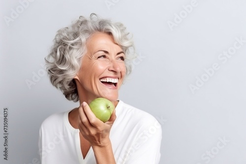 Beautiful cheerful smiling mature woman bites a green apple.