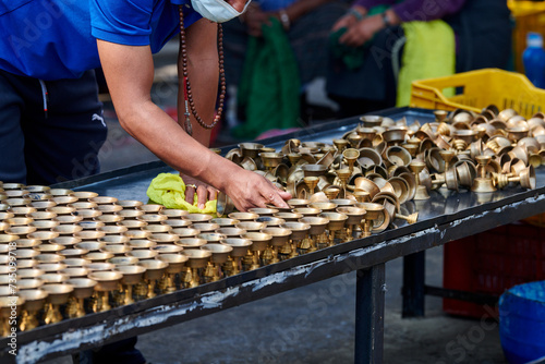 Nepali temple staff pour out candle oil after wick burns out for replacement, cleaning bronze candle holders reuse, volunteer work in for Boudhanath Stupa temple in Kathmandu photo