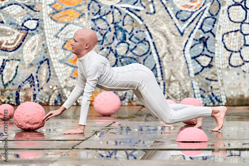 Outdoor dance of young ballerina girl with alopecia in white futuristic suit with plastic and flexible movements among pink spheres on abstract mosaic Soviet background, symbolizes self expression