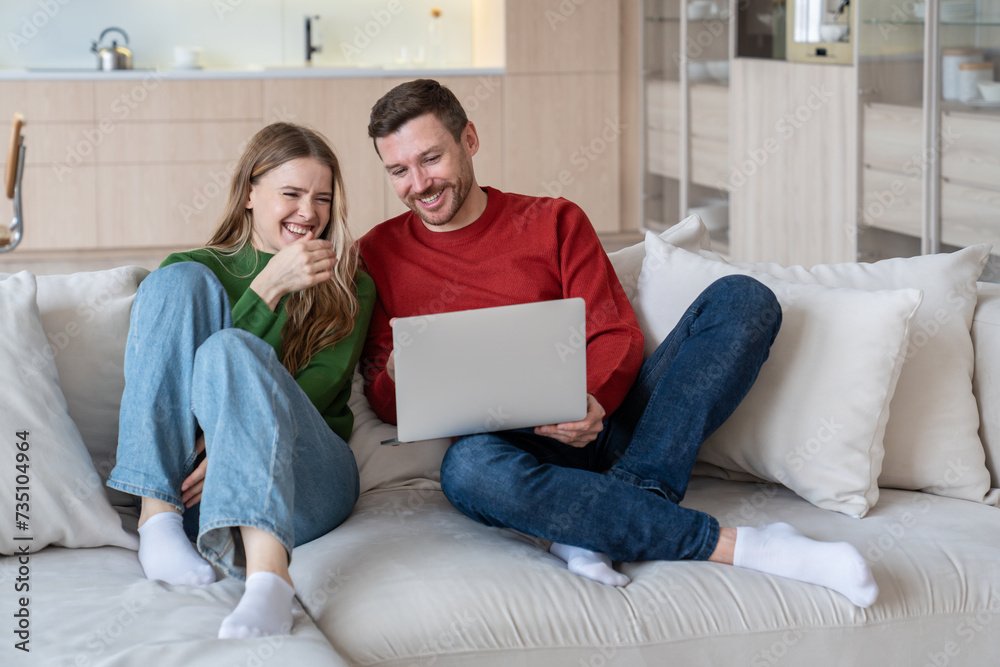 Glad joyful married couple laughing happily, looking into laptop computer screen. Cheerful wife and husband staying at home during lockdown, spending time together, watching comedies, funny videos Glad joyful married couple laughing happily, looking into laptop computer screen. Cheerful wife and husband staying at home during lockdown, spending time together, watching comedies, funny videos