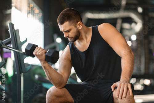 Bearded Male Athlete Making Seated Biceps Curl Exercise At Gym photo