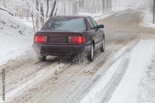 Loose snow in motion flies from under the wheels of a car on the road in the city. Blur. Dangerous driving conditions. Concept of safe driving on winter slippery road.