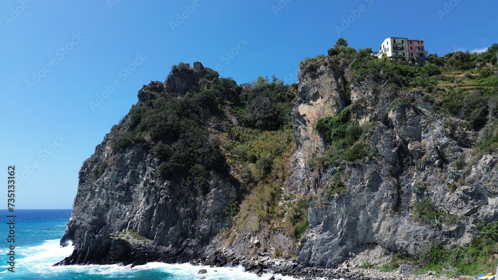 Coastal cliffs with lush greenery against the backdrop of a blue sky. Cinque Terre, Italy