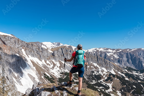 Hiker woman with panoramic view of majestic mountain peak Ringkamp in wild Hochschwab massif, Styria, Austria. Scenic hiking trail in remote Austrian Alps on sunny day. Wanderlust in alpine spring photo