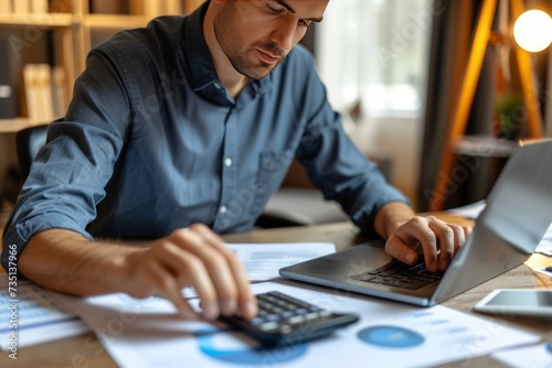 Professional business accountant working in office. Man in shirt sitting at his desk, doing paperwork, working on financial documents, using a laptop computer and checking some numbers on a calculator
