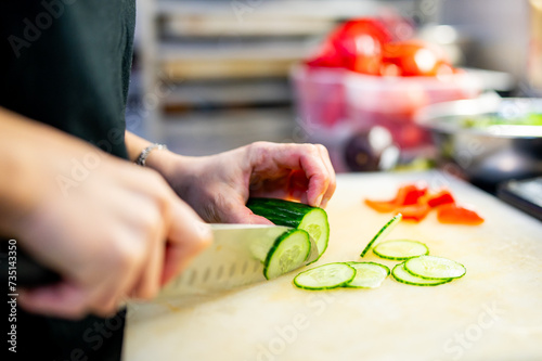 woman hands in disposable gloves slicing cucumber on cutting board.