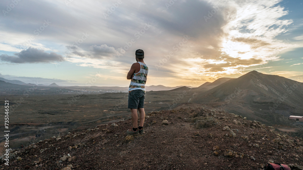 A man admires the view from the top of the mountain at the sunset after climbing a crater and reaching the top of a volcano in Fuerteventura, Canary Islands.