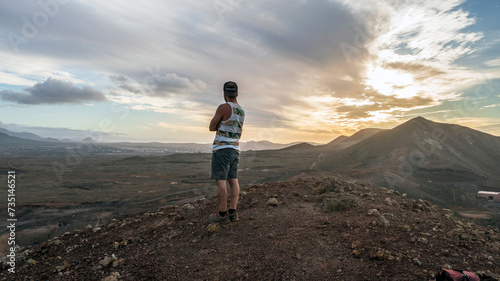 A man admires the view from the top of the mountain at the sunset after climbing a crater and reaching the top of a volcano in Fuerteventura, Canary Islands.