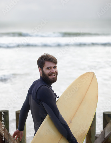 Happy man, portrait and surfer on beach for fitness, sport or waves on shore in outdoor exercise. Young male person with smile and surfboard for surfing challenge or hobby on ocean coast in nature