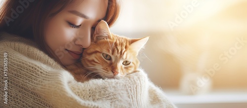 Young asian woman wears warm sweater resting with tabby cat on sofa at home one autumn day Indoor shot of amazing lady holding ginger pet Morning sleep time at home Soft focus. Creative Banner