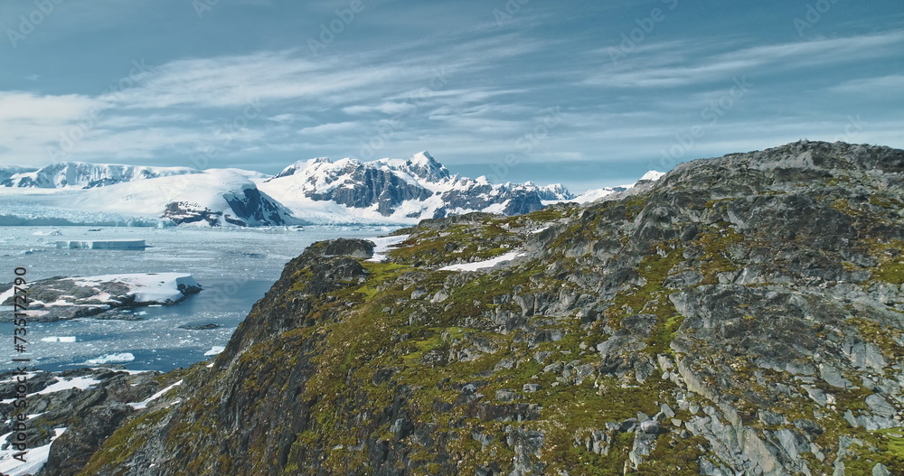 Green mountain at Antarctic ocean bay aerial view. Amazing nature of greenery rock at snow covered icebergs background. Birds flying over mount top. Environment scenery of climate change drone shot Green mountain at Antarctic ocean bay aerial view. Amazing nature of greenery rock at snow covered icebergs background. Birds flying over mount top. Environment scenery of climate change drone shot