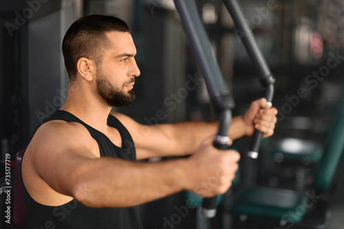 Portrait Of Motivated Muscular Man Training On Sport Machine At Gym