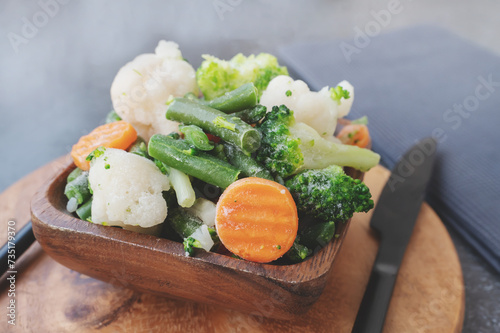 frozen vegetables. Wooden eco-friendly bowl with frozen vegetables on the table, green peas, carrots, cauliflower, green beans. Vegetable preservation concept.