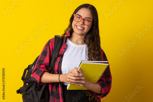 Woman wearing glasses, plaid shirt holding books and notebook with a backpack on her back