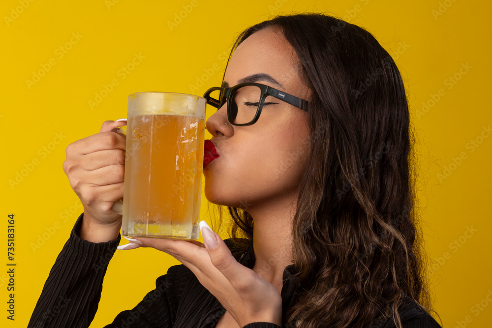 Sexy woman with long curly hair wearing a black textured outfit and holding a glass of cold beer