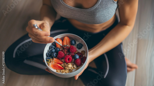 Vista superior de uma jovem em roupas esportivas tomando café da manhã saudável com granola e frutas frescas. photo