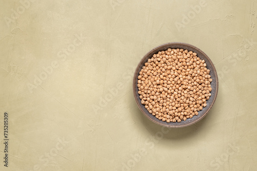Raw dry chickpeas in a bowl on a beige plaster background. Top view, copping space.