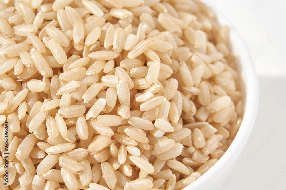 A bowl of uncooked brown rice, isolated against a white background. Healthy, savory dish includes whole grains like jasmine and basmati, showcasing a dieting Asian cuisine. A bowl of uncooked brown rice, isolated against a white background. Healthy, savory dish includes whole grains like jasmine and basmati, showcasing a dieting Asian cuisine.