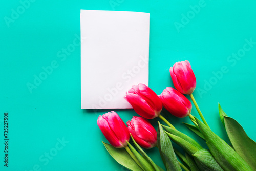 Fototapeta Naklejka Na Ścianę i Meble -  Bouquet of red tulips and white mockup blank on bright green background, copy space for the text