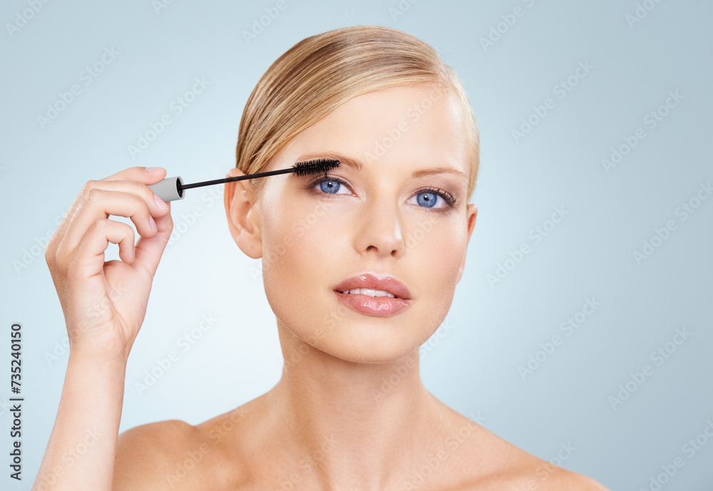 Beauty, mascara and portrait of woman in studio with confidence, makeup for lashes or facial glow. Glamour, cosmetics and face of girl on blue background with healthy skin shine, brush and wellness.