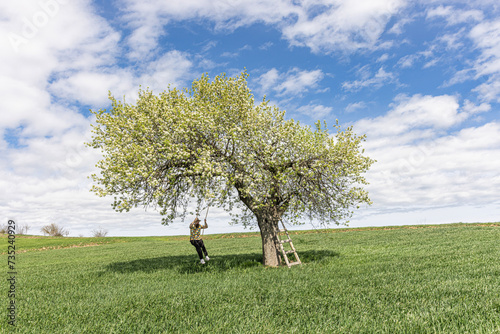 Young men swinging on a swing in a pear tree. Wooden swing on which a happy men swings outdoors. Swinging on a swing, dreaming of flying. Travel in nature in spring and summer. Healthy lifestyle.