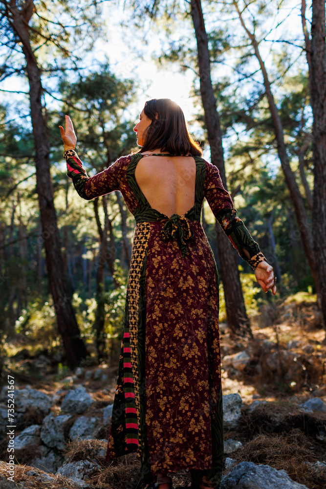 Young beautiful woman dancing in the forest with her hand raised.