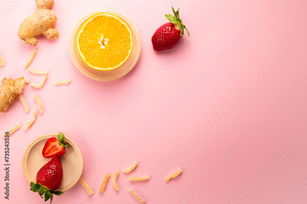 Ginger in sugar, strawberries and orange on pink background. Gourmet oriental sweets. Flat lay. Copy space