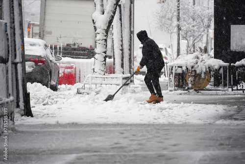 Fototapeta Naklejka Na Ścianę i Meble -  Small business owner or employee outside store shoveling ice and slush on downtown city street with falling snow