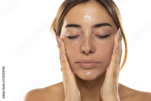 Young beautiful woman applying cream on her face on a white background