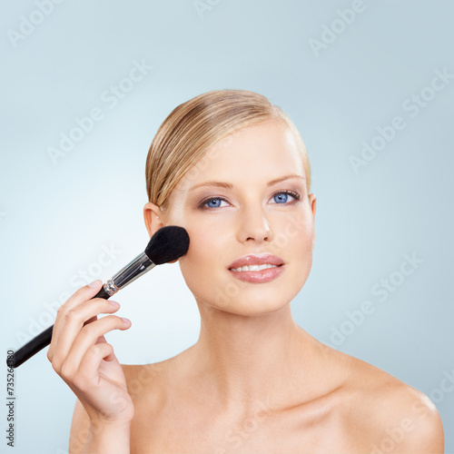 Cosmetics, brush and portrait of woman in studio with confidence, natural makeup or facial glow. Glamour, cosmetics and happy face of girl on blue background with healthy skin, shine and wellness.