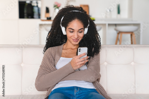 Young african woman female student using cellphone for listening to the music, favorite podcast radio on payed application subscription at home photo