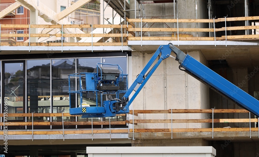 Blue cherry picker at work on the facade of a new building under construction. Blue cherry picker at work on the facade of a new building under construction.