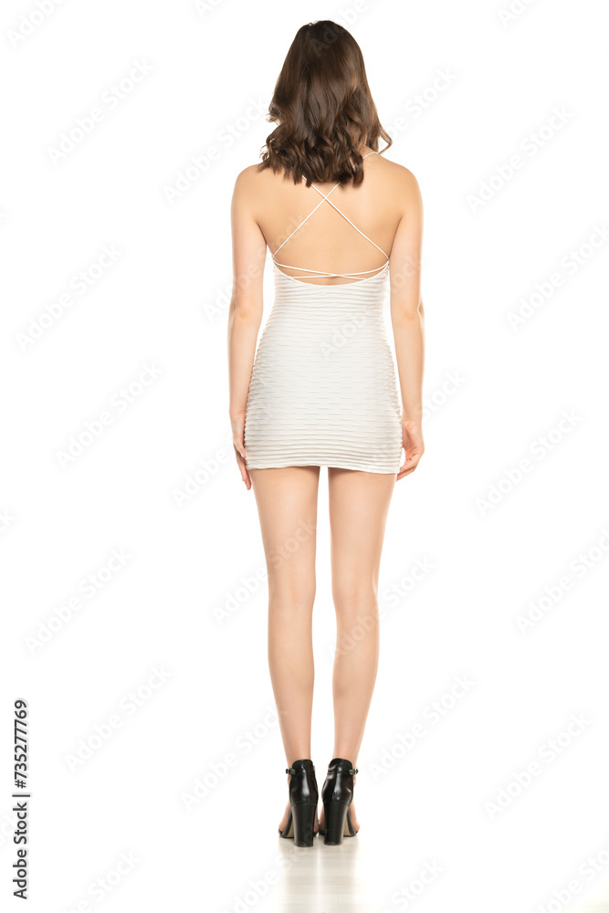 Summer Chic: Full-Length Portrait of a Young Woman Posing in a Short White Dress and Sandals on White Background. Back, Rear view Summer Chic: Full-Length Portrait of a Young Woman Posing in a Short White Dress and Sandals on White Background. Back, Rear view