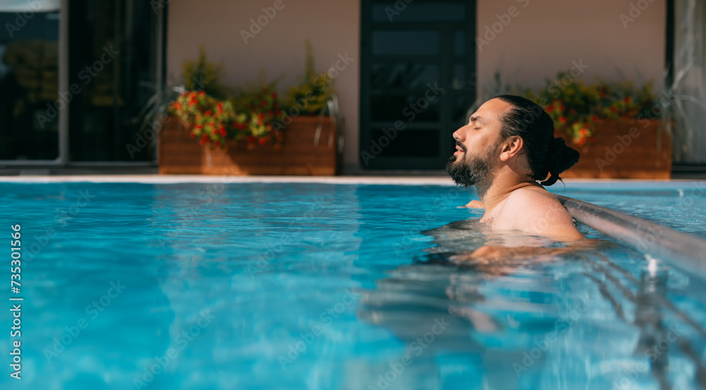 A young man is relaxing in an outdoor pool on a sunny day.