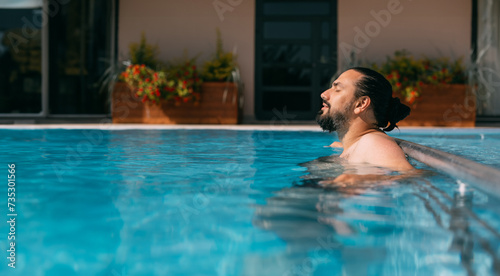A young man is relaxing in an outdoor pool on a sunny day.